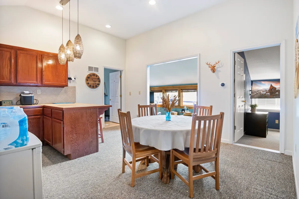 A cozy dining area featuring a wooden dining table, light fixtures, and a nearby kitchen island. The setup invites family meals, social gatherings, and the creation of new recipes, reinforcing the communal aspect of the kitchen-dining experience.