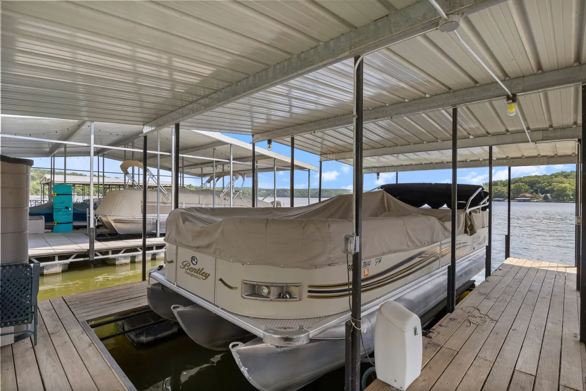 A covered pontoon boat rests at the dock, surrounded by calm water and lush greenery. The inviting dock provides direct access for boating adventures and relaxing breaks between water activities.