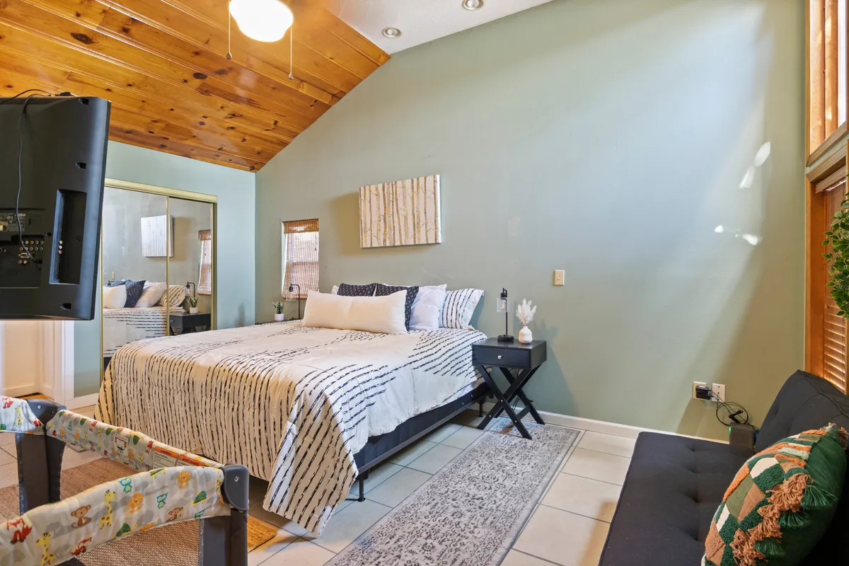 A spacious bedroom with a king-size bed, decorative artwork, a futon, and a bedside table. The space is designed for comfort, offering spots for both lounging and sleeping, as well as natural light for reading and relaxing.