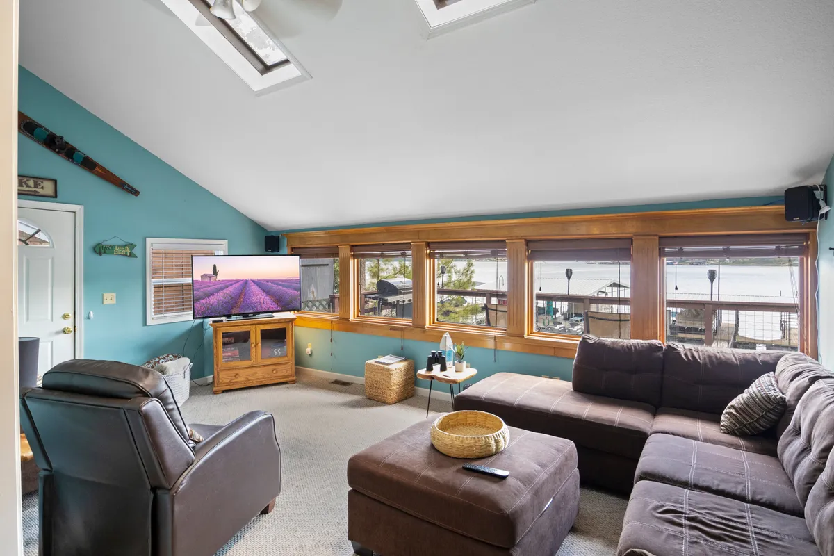 The living area showcases an expansive sectional sofa oriented towards a TV, with floor-to-ceiling windows framing a stunning view of the water. The cozy atmosphere is ideal for relaxing with family and friends, enjoying sunsets, or watching movies together.
