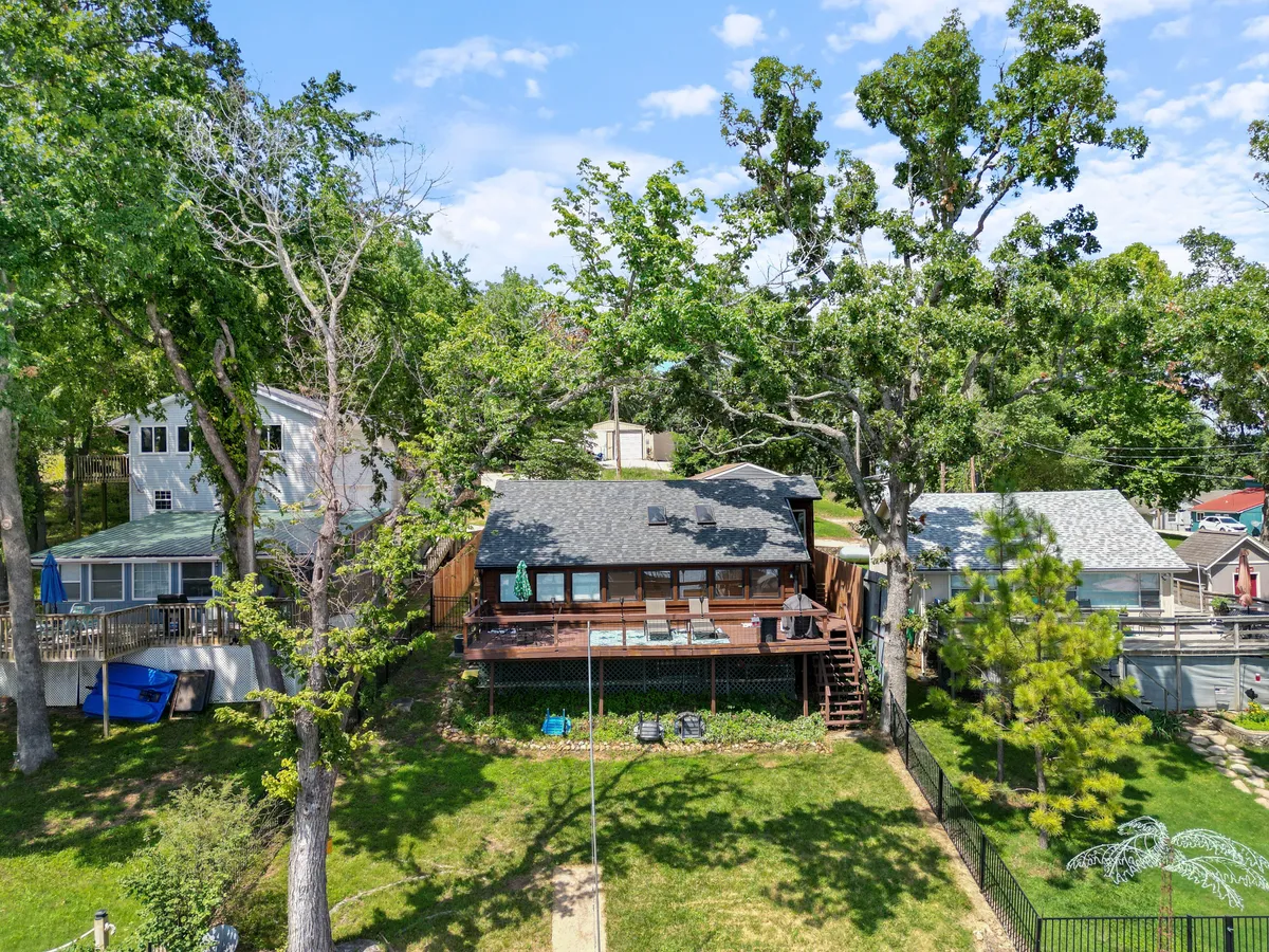 An exterior view of the home’s spacious wooden deck, green lawn, and large shade trees, with neighboring houses in the background. The deck is set up for gatherings and relaxation, inviting families and pets to enjoy the outdoors in comfort.