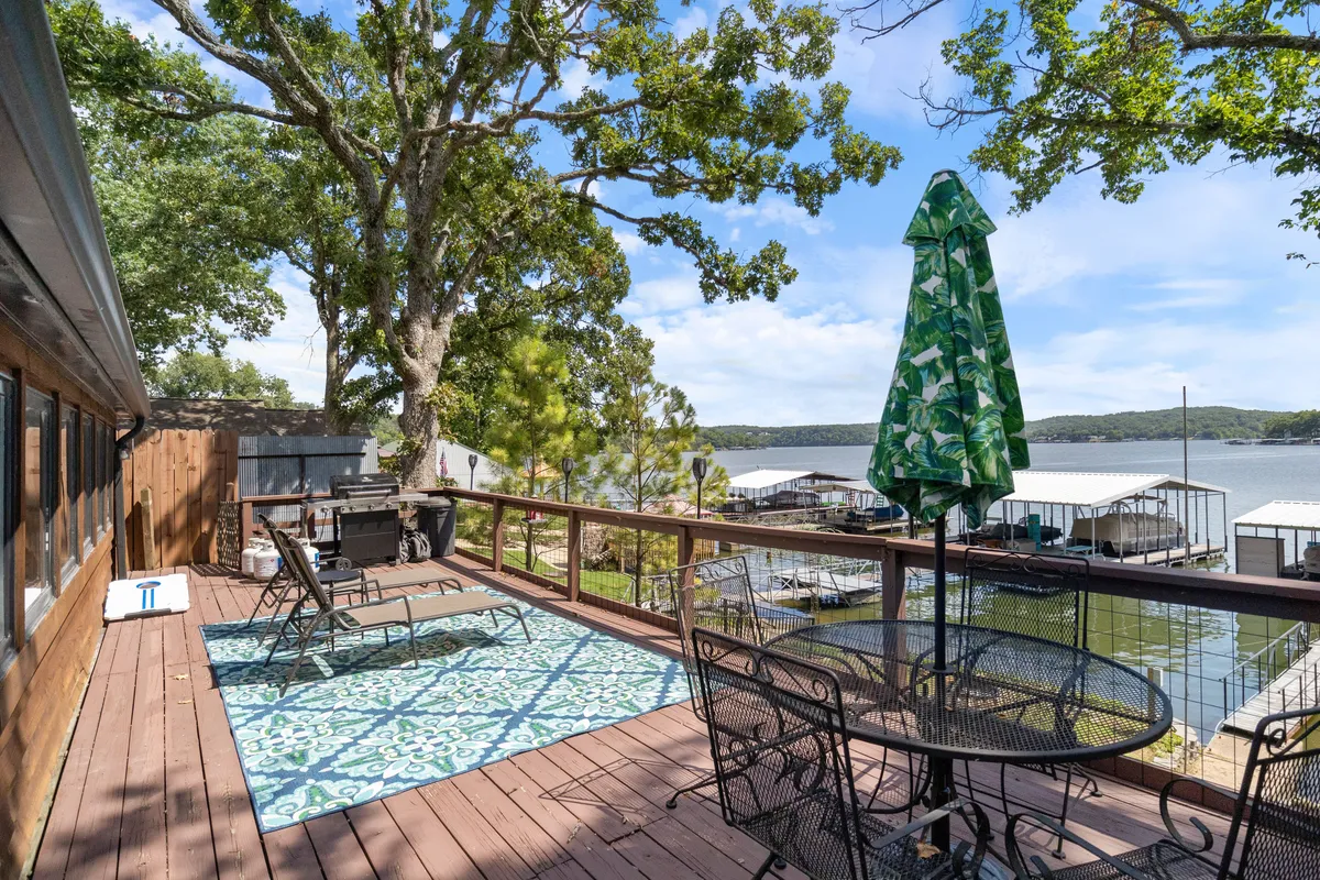The image captures a cozy outdoor seating area with a green umbrella, decorative rug, and a sweeping view of the lake. This setting suggests a casual, comfortable space for lakeside dining and relaxation, with the water providing a stunning backdrop.