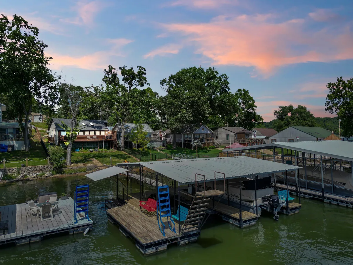 A wide shot of the dock area, showing the dock itself, boats moored alongside, nearby houses, and surrounding trees. The tranquil water invites aquatic activities and social gatherings, making it a hub for adventure and relaxation.