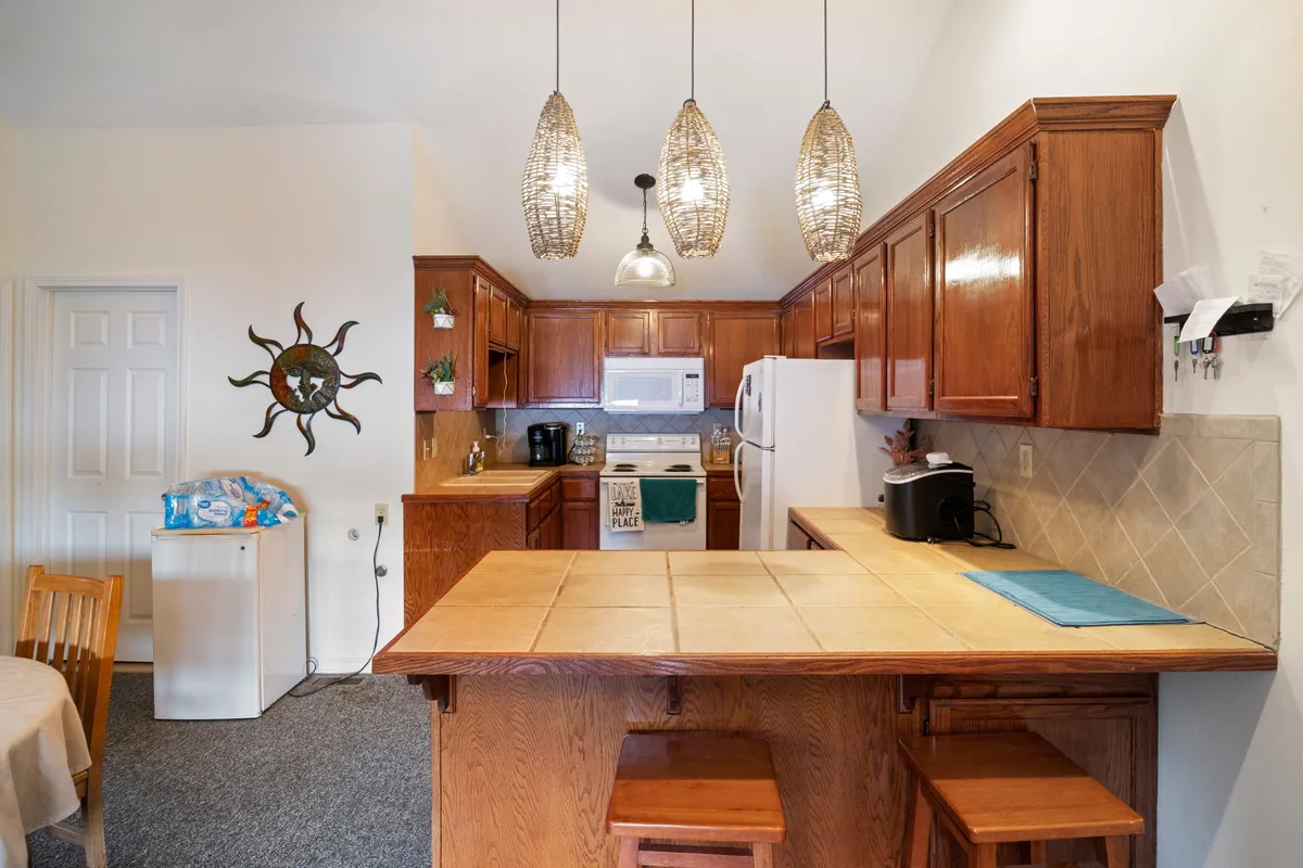 A warmly lit, open kitchen with a prominent island, hanging light fixtures, wooden cabinetry, modern appliances, and decorative wall art. The space is arranged for both cooking and entertaining, with an atmosphere that invites family gatherings and casual dining.