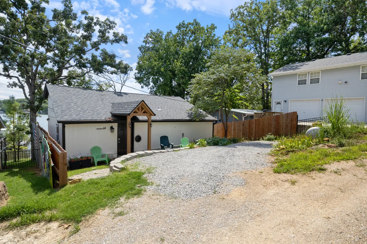 The image shows a welcoming entrance adorned with a decorative archway, green lawn chairs set on the grass, and a gravel driveway. The peaceful outdoor setting is perfect for relaxing with pets and provides a strong sense of arrival at a comfortable, well-maintained home.