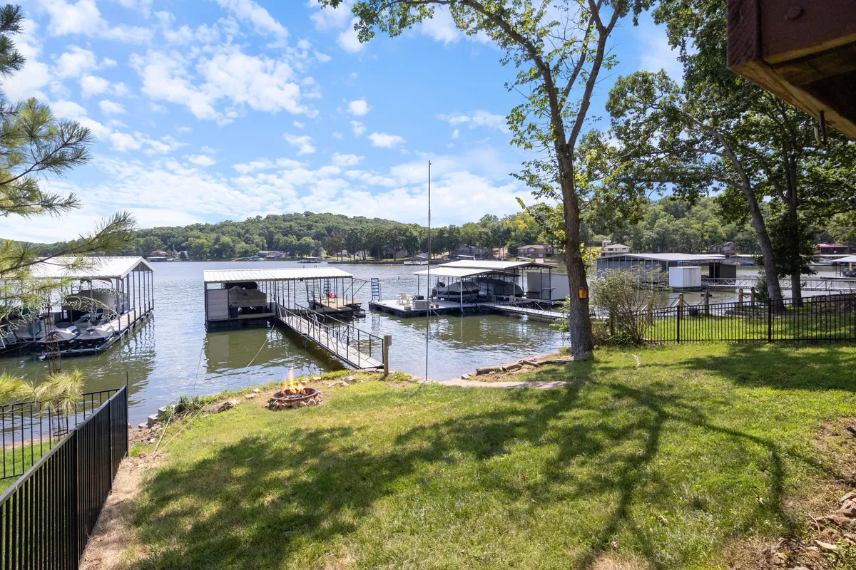A broad view of the lake shows multiple docks, a fire pit, and tree-shaded shoreline—an inviting space for gathering, lakeside dining, or winding down by the fire after a day on the water.